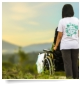 Ein eine Frau, die einen Rollstuhl durch die Landschaft schiebt.